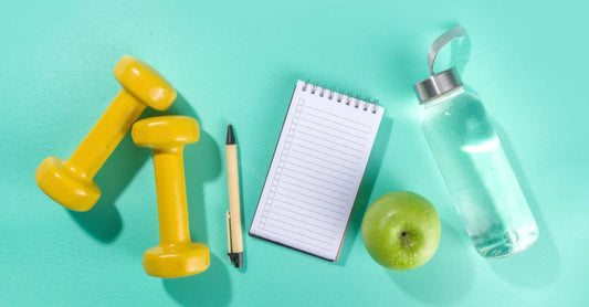 Taking Mounjaro for weight loss? Here’s how it may affect your libido, self-esteem, and sex life—and why sexual wellness should be part of your mental health journey. Dumb bells and pen next to a writing pad, a bottle of water and an apple.
